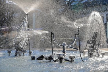 Basel, Switzerland - Feburary 07, 2023: The artistic Tinguely Fountain in the city center with partly frozen parts and splashing in backlit in cold winter weather