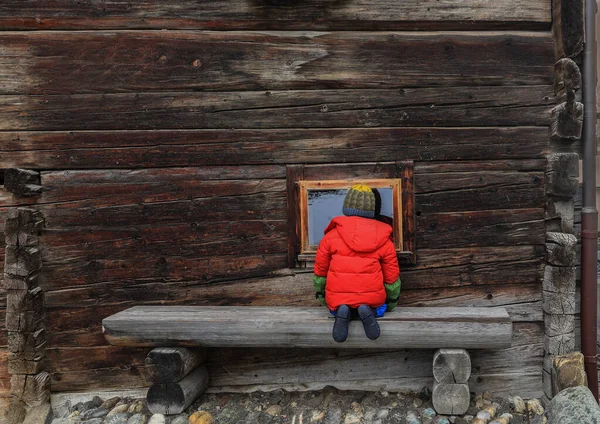 一个无法辨认的蹒跚学步的小孩好奇地朝一个木制谷仓的窗户看了看 — 图库照片