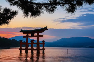Japon geleneksel kırmızı Torii tapınağı üzerinde gün batımı Itsukushima, Miyajima Adası nehrinde duruyor.