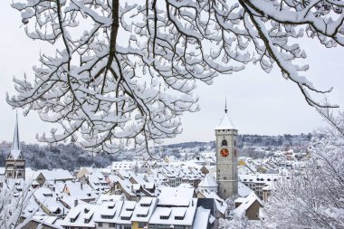 İsviçre 'nin Schaffhausen kentinde kar yağdıktan sonra eski kasabanın çatıları üzerindeki St. Johan kilise kulesi.