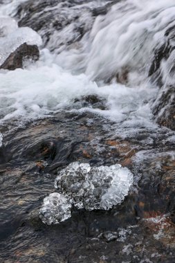 Kışın bir dağ şelalesinin ön planında kristal buz bloğu Sorvagen Şelalesi, Lofoten