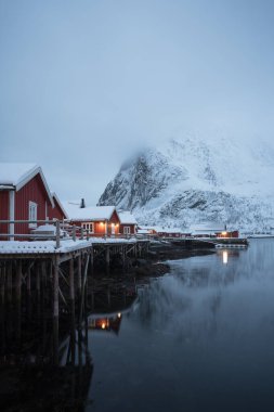 Geleneksel Norveç balıkçıları kış sabahları Norveçli Lofoten dağında sisli kırmızı kulübeler