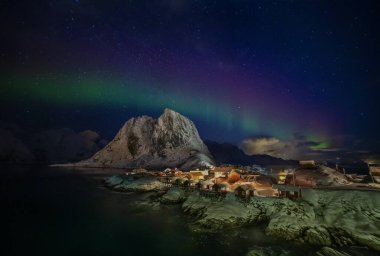 Hamnoy, Lofoten, Norveç 'te geleneksel kırmızı kulübeleri olan balıkçı köyünün üzerinde Aurora borealis.
