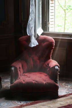 Red armchair in an abandoned room with light beams from the brocken window clipart