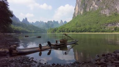 Guilin 'deki Li Nehri boyunca uzanan Karsten Dağı' nın manzarası. Üzerinde bambu salları ve iki komorant tünemiş.