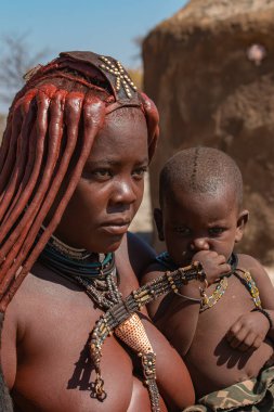 Damaraland, Namibya - 14 Temmuz 2024: Himba 'da bir köyde bebek tutan güzel bir Himba annesi. - Himba halkı Kuzey Namibya 'da yaşayan yerli bir kabiledir.