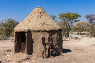 Damaraland, Namibya - 14 Temmuz 2024: Himba köyündeki çamurdan yapılmış kulübelerinin önünde iki genç çocuk. Himba halkı Kuzey Namibya 'da yaşayan yerli bir kabiledir.