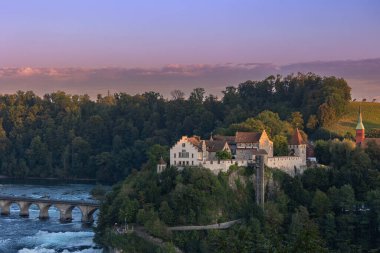 The medieaval castle Schloss Laufen over the biggest waterfall in Europe Rhinefalls in the sunset hours. clipart