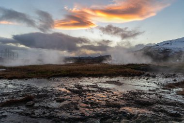 Günbatımında, Strokkur Geyser, İzlanda 'daki buharlı zeminde yansıyan termal manzara.
