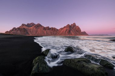 Vestrahorn ve siyah kumsal üzerinde günbatımı rengi ve Stoksnes, İzlanda 'da su sıçratan dalga. 