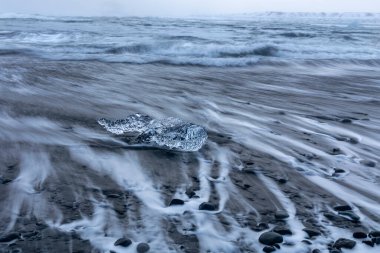 A single ice block with blurry waves from long exposure on the Diamond beach near Jokulsarlon lagoon, Iceland. clipart