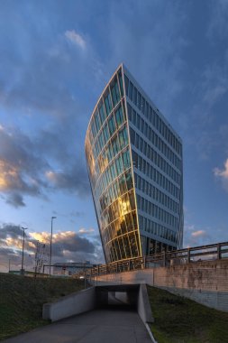 Kloten, İsviçre - Aralık 06. 2024: Modern eğik mimari Zürih havaalanındaki Çember cam cephede günbatımı yansıması ile.