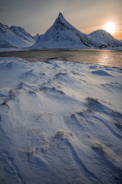 The famous mountain peak Volandstind at sunset time with snow field in foreground.  Lofoten, Norway, Norway clipart