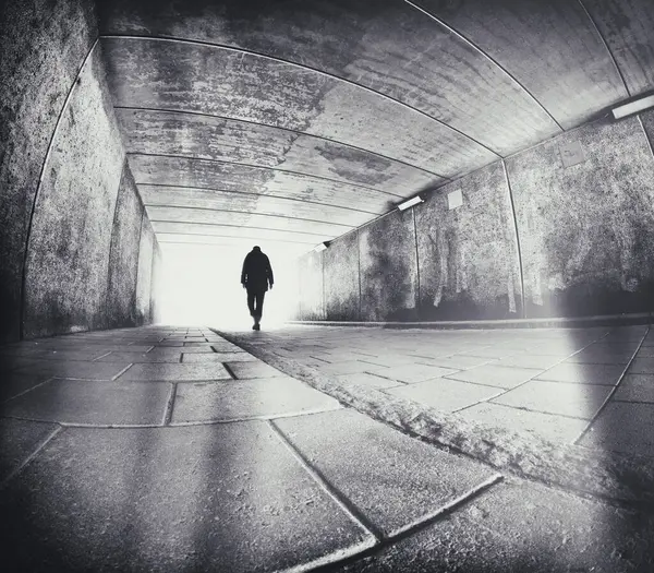 Silüetli hafif bükülmüş bir adam şehir beton tünelinde yürüyor..
