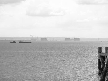 Bulutlu bir günde tek renkli sanayi kıyı şeridi manzarası kıyıda batık Hulk kalıntıları ve ön planda iskele.