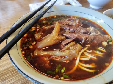 Braised beef noodle soup with chopsticks close-up.
