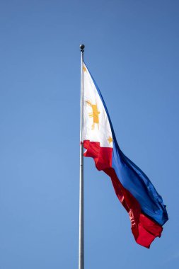 Filipinler bayrağı mavi gökyüzüne karşı rüzgarda dalgalanıyor.