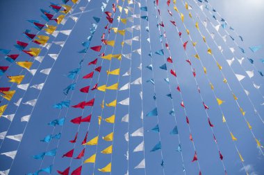 Mavi gökyüzünün altında dalgalanan renkli üçgen bayrak.