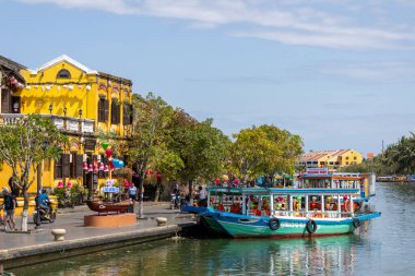 Hoi An, Vietnam- 1 Mar, 2024: Hoi An, Vietnam 'daki nehir boyunca turist parkı boyunca tekneler kullanılırdı. Hoi An, karma kültür ve mimarisi ile ünlü Dünya Kültür Mirası sitesidir..