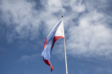 Filipinler bayrağı mavi gökyüzüne karşı rüzgarda dalgalanıyor.