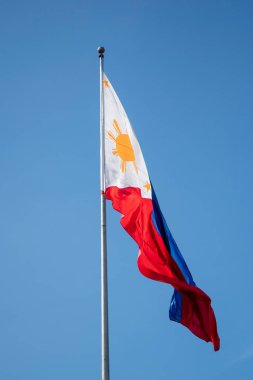 Filipinler bayrağı mavi gökyüzüne karşı rüzgarda dalgalanıyor.