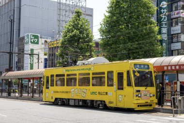 Okayama, Japonya - 10 Mayıs 2024: Okayama Elektrik Demiryolu tramvayı Okayama İstasyonu önündeki yolda ilerliyor.