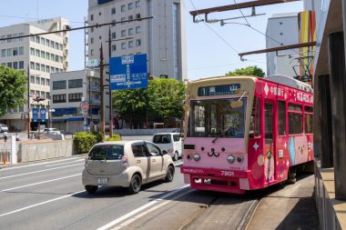 Okayama, Japonya - 10 Mayıs 2024: Okayama Elektrik Demiryolu tramvayı Okayama İstasyonu önündeki yolda ilerliyor.