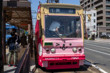 Okayama, Japonya - 10 Mayıs 2024: Okayama Elektrik Demiryolu tramvayı Okayama İstasyonu önündeki yolda ilerliyor.