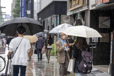 Tokyo, Japonya - 13 Mayıs 2024: Tokyo 'da yağmurlu bir günde insanlar şemsiyeyle sokakta yürür.