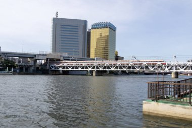 Tokyo, Japonya - 11 Mayıs 2024: Sumida Nehri 'nin karşısındaki Tokyo, Japonya' daki Sumida Nehri Yürüyüş Parkı 'nda demiryolu köprüsü. Sumida Nehri Yürüyüşü, nehrin kenarındaki çekimleri görmenin yapılandırılmış bir yoludur.
