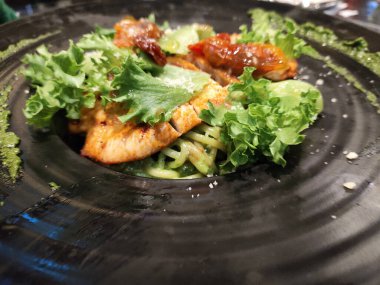 Izgara tavuklu makarna ve siyah tabakta fesleğen sosu.