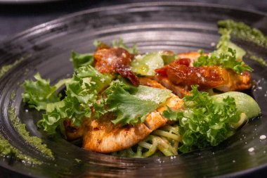 Izgara tavuklu makarna ve siyah tabakta fesleğen sosu.