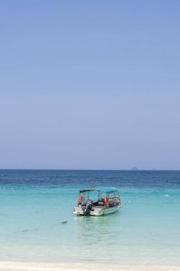 Redang Adası kıyısında kristal berrak su ve beyaz kumla dolu küçük bir tekne park ediyor.