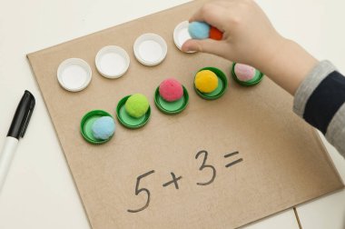 Plastik şişe kapakları. Doğru miktarda ponponu kupalara koy, matematiksel denklemi tamamla. Beş dakikalık el işi. Çocuk yuvası aktivitesi. Erken eğitim, sayma oyunu, iyi motor becerileri..