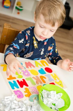 Tahta alfabe harfleriyle oynayan iki yaşında bir çocuk. Folyoya sarılı mektuplar. Entellektüel oyun, erken eğitim için anaokulu uygulaması. Sözlü ve bellek alıştırması.