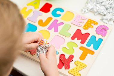 Tahta alfabe harfleriyle oynayan iki yaşında bir çocuk. Folyoya sarılı mektuplar. Entellektüel oyun, erken eğitim için anaokulu uygulaması. Sözlü ve bellek alıştırması.