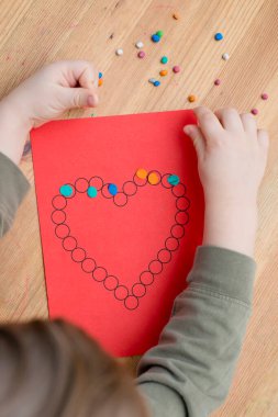 Annem için sevgililer günü tebrik kartı hazırlıyorum. Küçük çocuk baskılı kağıt kalbe hamur uyguluyor. Güzel motor beceriler, parmak koordinasyonu. bebekler için erken eğitim