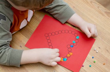 Annem için sevgililer günü tebrik kartı hazırlıyorum. Küçük çocuk baskılı kağıt kalbe hamur uyguluyor. Güzel motor beceriler, parmak koordinasyonu. bebekler için erken eğitim