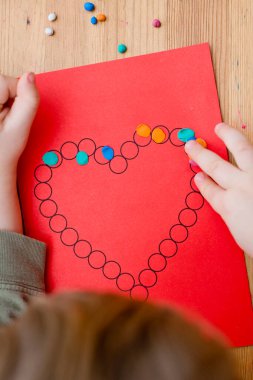 Annem için sevgililer günü tebrik kartı hazırlıyorum. Küçük çocuk baskılı kağıt kalbe hamur uyguluyor. Güzel motor beceriler, parmak koordinasyonu. bebekler için erken eğitim