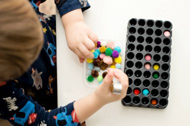 Sensory tool. Boy inserting pompons in beaker holder