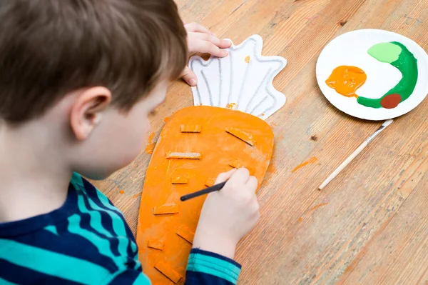 Second chance for packaging. Boy making a carrot from cardboard. Class for therapy of art. Fine motor skils, task of sensorics. Activities at home.