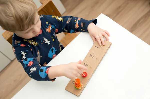 Home made tool for early education, fine motoric skills. 2 year old boy puts pasta on wooden rods. children, people, infancy and education concept. formation and development of the child.