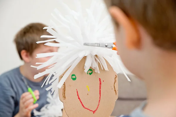 stock image Playing hairdressing saloon. Zero waste, reusing packaging materials. Customer doll made from used cardboard and PE foam. Boy cutting hair. Role-playing games at home.