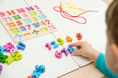 Çocuk oyun yoluyla numaraları öğreniyor. Tahta sayılar ve ayakkabı bağcıklarıyla duyusal aktivite. Evde eğitim, okul öncesi eğitim, Montessori metodolojisi. sayılar dizisi, aritmetik problemler.