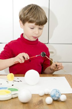 Okul için Güneş Sistemi 'nin modelini yaparken çocuk köpük topları boyuyor. Evde fen ödevi. Çocuklara öğretme kavramı. Erken yaştan itibaren yaratıcılığı gelişiyor. Fırça ve acıyla çiziyor.