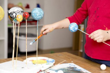 Okul için Güneş Sistemi 'nin modelini yaparken çocuk köpük topları boyuyor. Evde fen ödevi. Çocuklara öğretme kavramı. Erken yaştan itibaren yaratıcılığı gelişiyor. Fırça ve acıyla çiziyor.