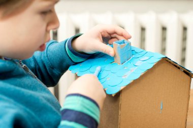 Küçük Mavi Kağıt Evi 'ni inşa eden çocuk. Evdeki etkinlikler. Anaokulu veya anaokulu öğretmenleri için yaratıcı fikirler. Özel ihtiyaçları olan insanlar için Montessori tematik aracı.