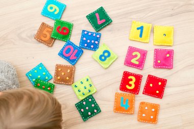 Yürüyen çocuk yerde oynuyor. Ev yapımı oyun: Doğru çifti bul. Farklı renkte doldurulmuş kare şeklinde sayılar ve eş domino benzeri noktalar. Erken eğitim, öğrenme rakamları.