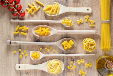 Kaşıklar, domatesler ve zeytinyağlı çeşitli makarnalar. Üst görünüm düzlüğü