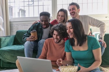 Dizüstü bilgisayar ile genç arkadaş bir grup kapalı kanepede oturan, film izlerken.